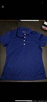 Blue women's golf polo shirt laid flat, showing front with collar and four white buttons
