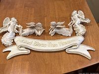Angel figurines and God Bless This House plaque laid on wooden surface.