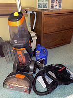 Full view of upright Bissell ProHeat 2X Revolution Pet carpet cleaner with cleaning solution bottle and accessories on floor next to it.