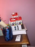 Photo showing Canon Pixma 245 ink cartridges on a desk with pens in a blue holder and a stack of paper.