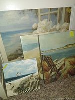 Four sea shore themed canvas prints arranged leaning against a wall, showing flowers, ocean and beach scenes.