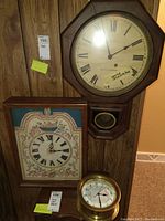 Photo showing three clocks: a Seth Thomas wall clock with octagonal wooden frame, a handcrafted needlepoint clock with floral face in rectangular wooden frame, and a small round tide clock with brass bezel.