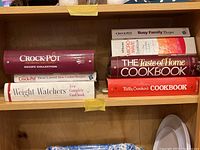 Shelf with 7 cookbooks including Betty Crocker's Cookbook, Crock-Pot Recipe Collection, Weight Watchers, Taste of Home, and more