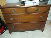 Front view of the wooden dresser showing four drawers with metal oval handles and visible scratches on the surface and drawer fronts.