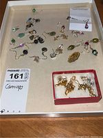 Full view of assorted pierced earrings on white tray, showing diversity in colors and styles with multiple earring pairs and singles scattered.