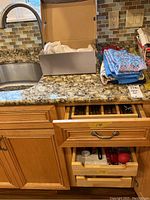 Opened kitchen drawers and counter showing folded kitchen towels and linens along with a shoebox containing flatware