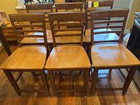 Set of six wooden bar-height kitchen chairs arranged in two rows, showing the front and side angles. Medium brown finish with three horizontal slats on backs, visible wear and scuffs on surfaces.