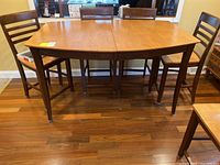 Front view of wooden bar height kitchen table with two chairs visible. Table has medium brown finish and shows general use wear.