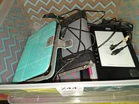 Several Kobo eReaders and tablet cases tangled with USB cables placed inside a container with a chevron pattern background