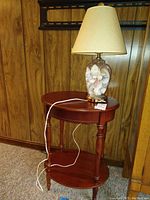 Front view of the wooden end table with shell-filled glass lamp on top showing leg and shelf details