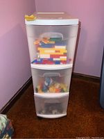 Three-tier plastic drawer unit containing assorted LEGO pieces visible inside semi-transparent drawers.