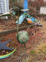 Metal bird sculpture with circular patterned body and long legs in garden mulch next to wooden border and other garden items.