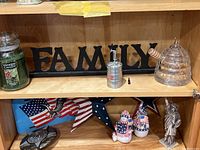 Shelf photo showing Yankee Candle, FAMILY plaque, crystal honeypot, miniature keg figure, and patriotic figures.