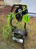 Front and top view of Greenworks power washer with coiled high-pressure hose and spray lance attached, showing 2000 PSI rating on machine.