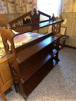 Front and angled view showing the entire wood bookshelf with three main shelves and a smaller top shelf with decorative back panel and side cutouts.