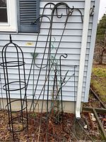 Full view of various metal garden structures against a house wall including shepherd's hooks and trellis.