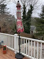 Full view of the table umbrella with stand on an outdoor wooden deck showing fabric pattern and stand base.