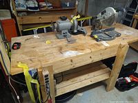 View of the wooden workbench showing the bench grinder and the miter saw secured with caution tape.