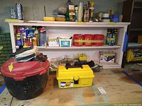 Red and black shop vacuum, yellow toolbox with hand tools, various cans and bottles of household repair products on shelves
