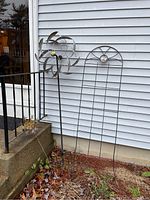 View of the metal trellis standing upright with the metal wind catcher beside it outdoors against a house exterior wall, showing overall appearance and scale.