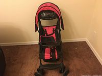 Front view of the Kolcraft baby stroller showing the pink and black padded seat, canopy, and front tray with cup holders.