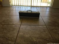 Closed black and silver hard carrying case for barbecue tools on tiled floor.