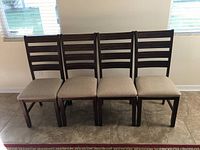 Front view of four dark wood dining chairs with beige upholstered seats arranged side by side on tiled floor.