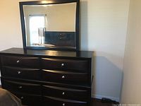 Front view of black wooden 8-drawer dresser with large attached mirror, showing drawers with round silver knobs and overall condition.