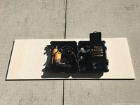 Bostitch drill and drill bit set inside black metal case on light wood board outdoors