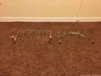 Two metal over the door hangers lying on carpet, one straight bar with 7 hooks, one decorative scroll design with 7 hooks, showing overall condition and design.