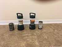 Four battery-powered lanterns lined up on tile floor showing differences in size and design.