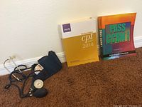 Front view of two nurse practitioner study books and manual blood pressure machine on carpet with brown background.