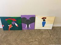 Three canvas paintings placed side by side on the floor showing koi fish, elephant face, and vase with flowers.