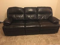 Front view of the dark brown leather recliner sofa, showing three seats and padded armrests.