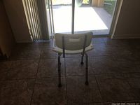 Back view of the shower chair showing white plastic backrest and metal legs with rubber tips