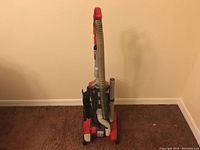 Full view of red Dirt Devil upright vacuum cleaner with hose and cord wrapped on back.