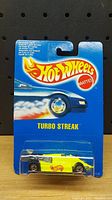 Front view of sealed Hot Wheels Turbo Streak 2 toy car in original blister pack with blue backing card and yellow car with red flame logo visible.