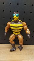 Front view of Buzz-Off Masters of the Universe figure, showing yellow and black striped torso and muscular arms.