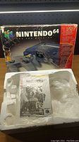 Nintendo 64 retail box with visible wear and tear beside styrofoam foam packaging insert and plastic wrap residues.