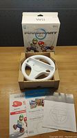 Front view of the Nintendo Wii Mario Kart steering wheel in its open box with manual and inserts.