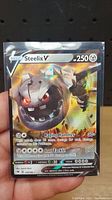 Front side of Steelix V Pokemon trading card showing holographic design with attack details.