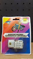 Photo of vintage white diecast metal Rescue Patrol jeep toy in original blister pack with colorful background and rescue patrol graphics