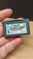 Front of the Super Mario World Super Mario Advance 2 cartridge held in hand showing label and game title.