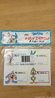 Front photo showing sealed package of Tiny Toons Happy Birthday & Name Tags with 8 tags featuring characters Babs Bunny, Buster Bunny, Plucky Duck, and Dizzy Devil
