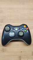 Front view of black Xbox 360 wireless controller with visible buttons and analog sticks.