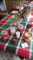 Lot with the green-etched hurricane glass and the seven assorted candles on a holiday-themed tablecloth.
