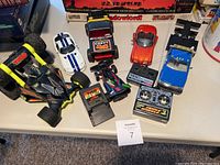 Six assorted kids' cars displayed on a table including a large Tyco remote control car, five other cars, and the remote controller.