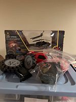 Remote control helicopter in black box, red remote control car with loose parts in plastic bag in front.