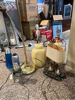 Group of five assorted lamps including lava lamps and vintage styles without shades, displayed on carpeted floor beside boxes and household items