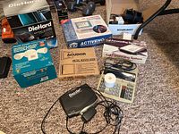 Photo showing boxed DieHard Battery Charger, Heath Zenith Motion Sensing Halogen Light box, Acudor Metal Access Door box, ActiveHot Call Forwarding System boxes, calculator, and Dazzle video device on carpet.